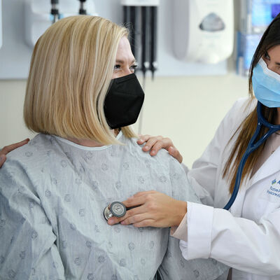 A female physician assistant student using a stethoscope on a patient