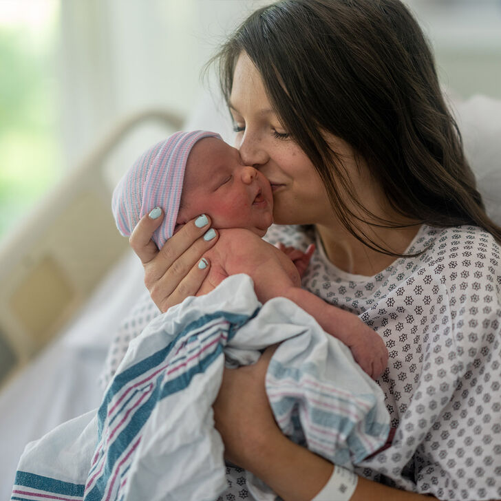 A mother kisses her newborn baby in a delivery room