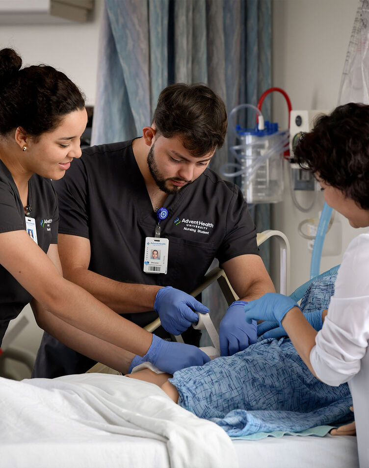 Two nursing students practice their skills on a simulator with faculty guidance.